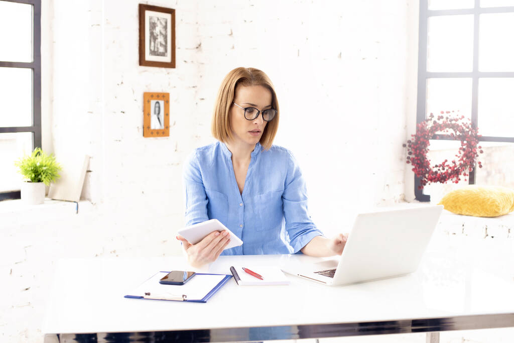Egy nő ül az asztalnál, laptoppal, Kékfény szűrőszemüveget visel.